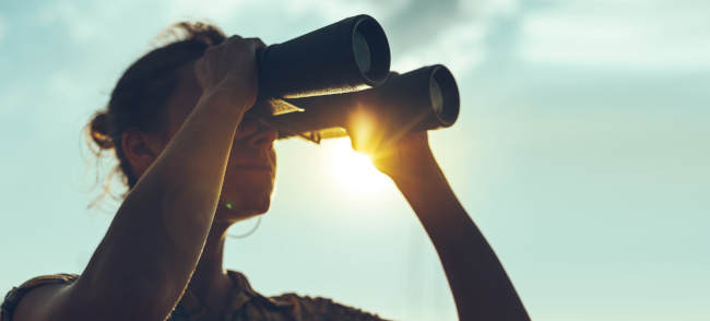 Junge Frau guckt durch Fernglas im Gegenlicht